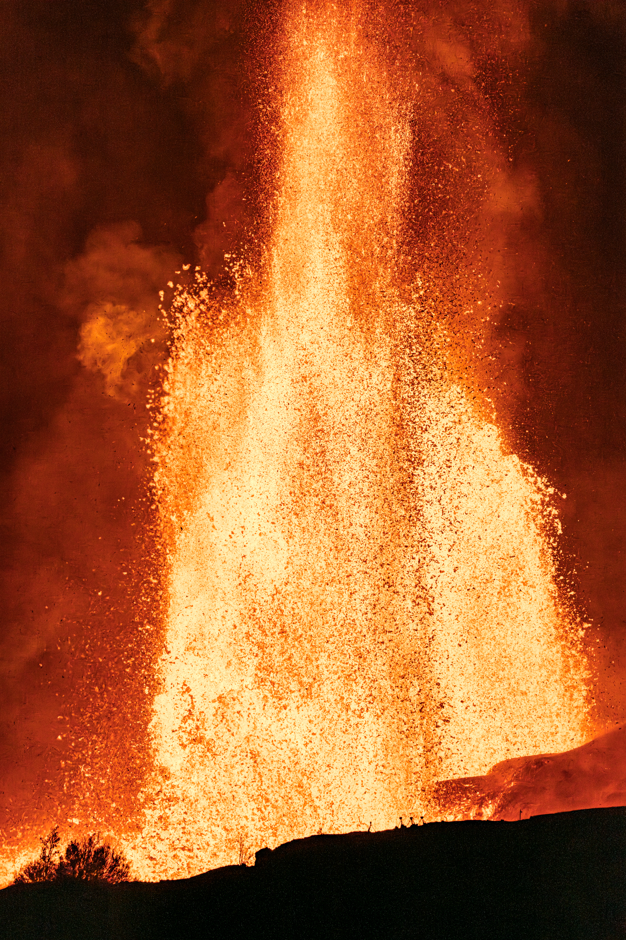 A tall column of orange lava and sparks rises behind a dark ridge.